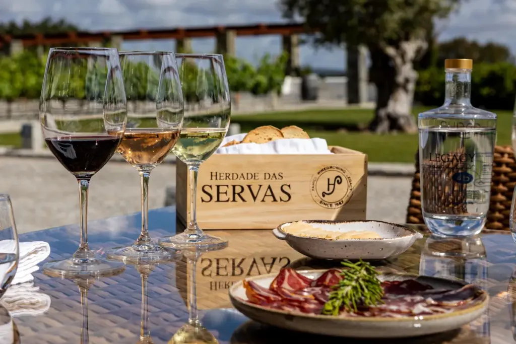 Copos de vinho branco e tinto, tábua de presunto e caixa de vinho Herdade das Servas no welcome drink